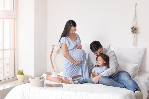 Happy man laying on bed with his daughter and pregnant wife at home