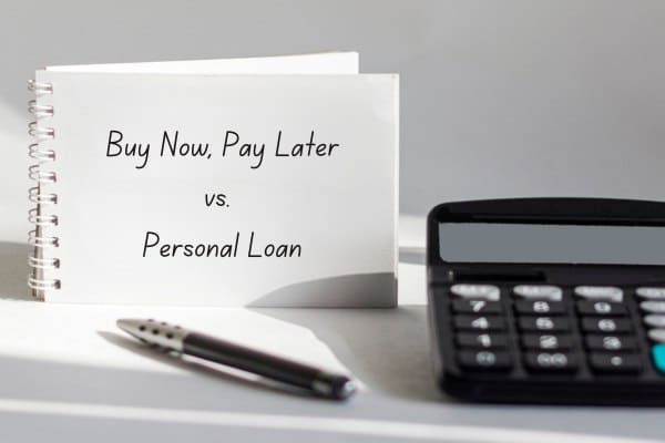 Words "Buy Now Pay Later vs. Personal Loan" on a notebook with a pen and calculator on a table